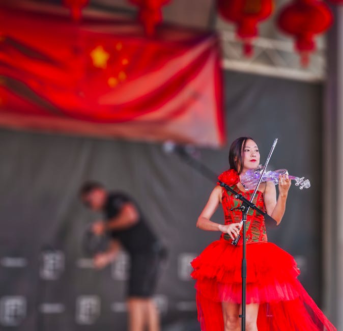 A talented violinist performs on stage in a vibrant red dress during a cultural festival.